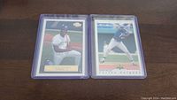 Two Carlos Delgado rookie baseball cards in clear protective sleeves placed side by side on a wooden surface.