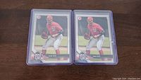 Two Juan Soto rookie baseball cards in blue protective cases placed side by side on a dark wooden surface.