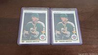 Two Mike Modano rookie hockey cards in protective sleeves placed on wooden surface.