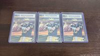 Photo showing three Tom Brady football cards in Michigan uniform, all in plastic sleeves.