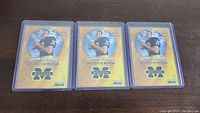 Three Tom Brady University of Michigan football cards in protective plastic holders displayed side by side on flat surface