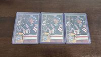 Three Tony Amonte rookie hockey cards in individual protective plastic cases placed on a wooden surface.