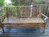 Front view of bamboo bench showing slatted seat, lattice style backrest, weathered surface, and solid bamboo frame and legs.