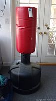 Photo of the full freestanding Wave Master punching bag with red striking pad and black base, shown indoors near glass doors.