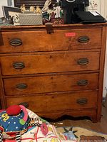Front view of vintage wooden dresser showing four drawers with oval recessed metal handles and worn wood surface with scratches.
