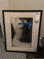 Photo of black framed nude photo print with blue tape across chest, showing female torso side view