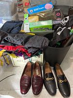 Photo showing two pairs of men's leather shoes, Mardi Gras masks, colorful fabric costumes, a pool float box, and various costume props in a bin