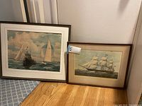 Two framed nautical-themed prints positioned on the floor showing tall ships and sailing vessels.