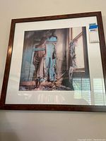 Front view of framed photography print showing a woman standing in a peeling wall interior with window and floral curtains