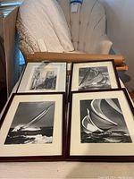 Four framed prints laid out on a surface: three sailing scenes in dark wood frames and one cathedral engraving in a black frame.