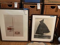 Two framed sailing themed artworks side by side on floor in front of wicker baskets