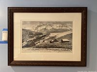 Framed black and white landscape print showing mountains and buildings in a rural setting, with signature visible.