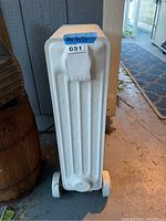 Photo from side showing white electric oil-filled space heater radiator with wheels and control knob.