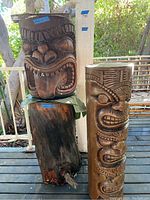Front view of two carved Tiki statues stacked on the stump on a deck