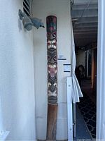 Full view of the carved wooden totem pole against a white wall, showing entire height and base
