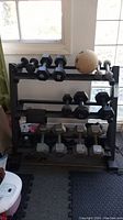 Overall view of dumbbells on the three-tier metal rack with medicine ball on top