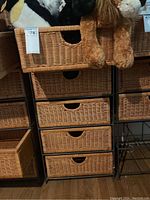 Front view showing the wicker chest of drawers with five basket drawers supported on a black metal frame alongside adjacent furniture.