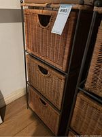 Side view of wicker chest of drawers showing three woven baskets and metal frame with auction tag attached.
