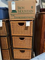Frontal view of wicker chest showing three woven drawers and a metal frame, with a cardboard box on top.