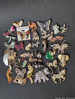 Full assortment of animal and insect figural brooches laid out on black surface showing variety of designs and colors