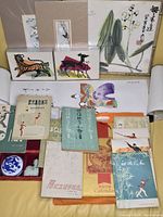 Overall view of assorted Asian artwork prints, books primarily on Tai Chi, a novelty calendar, and more arranged on a surface.