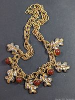Full view of gold tone chain necklace with acorn and oak leaf charms, laid flat showing overall design and length.