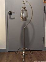 Full view of tall chrome hanging stand with the lantern suspended from the top hook. Stand has a claw foot base and is metal with a shiny chrome finish showing some tarnishing.