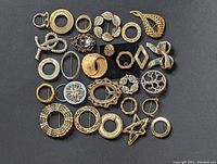 Top view showing an assortment of gold and silver tone circular and abstract shape brooches arranged closely together on a white surface.
