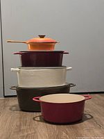 Side view of stacked enameled cast iron Dutch oven pots of various colors showing height and shape.