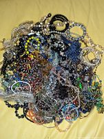 Top-down photo of a tangled bulk bag of assorted faceted crystal jewelry including many beaded necklaces and bracelets in various colors on a yellow background.