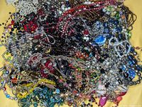 Overhead view of a plastic box filled with a tangled assortment of crystal bead necklaces and silver chain jewelry in various colors including blue, red, green, white, brown, black and more.