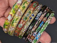 Close-up photo of nine thick enamel cloisonné bangle bracelets held together showing detailed floral designs in vibrant colors with gold outlines.