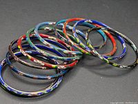 Ten thin enamel cloisonné bangles arranged overlapping, showing variety of colors and patterns.