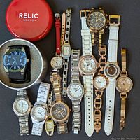 Image showing all 11 watches arranged on a dark surface, including various metal, resin and leather bands, with some in red and white cases