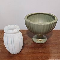 Two vases on wooden surface: a green Haeger ceramic footed vase and a white alabaster Vero Italy bud vase with blue stripes.
