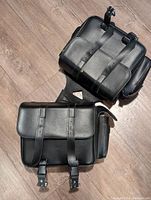 Top view of two black leather motorcycle saddle bags showing buckle straps and front flap closure.