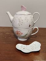 Full view of Lenox Butterfly Meadow porcelain tea set stacked showing teapot with butterfly lid, teacup, and small dish in front