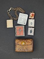 Miniature leather book, religious lockets including cross motif, double photo locket on chain, small photo lockets, and brown leather pouch.