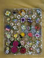 Full view of assorted porcelain floral jewelry set arranged in plastic tray showing a variety of colors and flower designs
