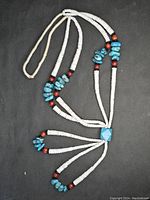 Full view of the necklace showing the white shell disc beads, turquoise nugget beads, red coral, and black spacers with a distinctive Jacla design with fringe strands.