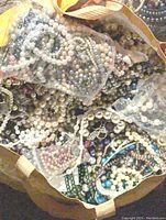 Full view of tote filled with numerous strands and loose pieces of faux pearl jewelry, some contained in small mesh bags, showing varied colors and sizes.