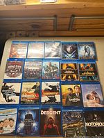 Photo showing entire set of 20 Blu-Ray DVDs laid out in a grid pattern on a wooden surface including action and thriller movie titles.