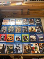 Full layout of 24 Blu-ray DVD movie cases arranged on a flat surface showing various titles including Fast & Furious, Bourne series, Resident Evil, and Sherlock Holmes.