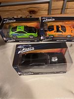 Photo showing all three Fast & Furious die cast cars in original packaging: green Mitsubishi Eclipse, orange Toyota Supra, and black Dodge Charger.