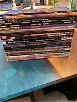 Photo of the spines of 22 soft cover comics and graphic novels stacked vertically showing all titles and publishers.