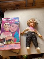 Photo showing the original box packaging of the 1990 Michelle Doll from Full House beside the doll lying on a surface.