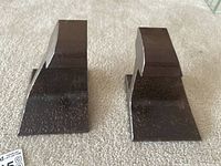 Pair of metal Brutalist style bookends placed on a carpeted floor, showing their overall shape and size from a front angle.
