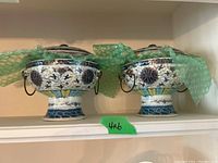 Two covered pedestal bowls side by side on shelf
