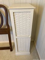 Front view of the tall narrow cabinet showing the woven wicker door panel and white painted wood frame.