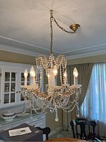 Full view of the chandelier hanging from the ceiling with chain and canopy, showing six lit light bulbs shaped like candles with glass bobeches and multiple strands of glass beads.